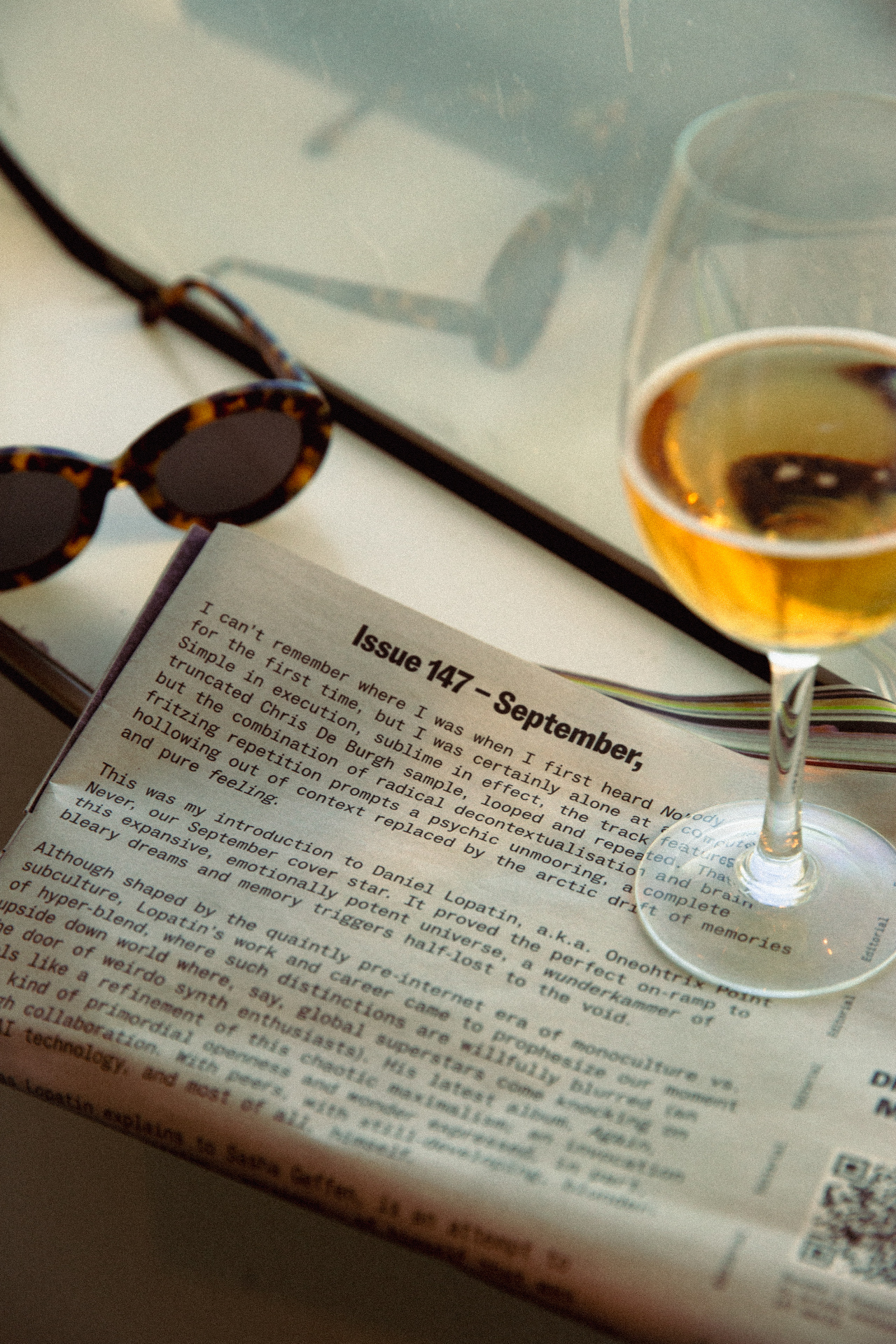 An open magazine, sunglasses and a glass on a sunlit table